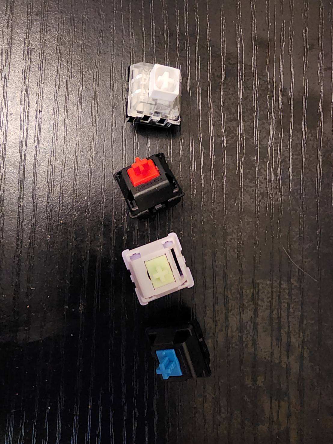 An image of four different mechanical keyboard switches lying on a black desk.